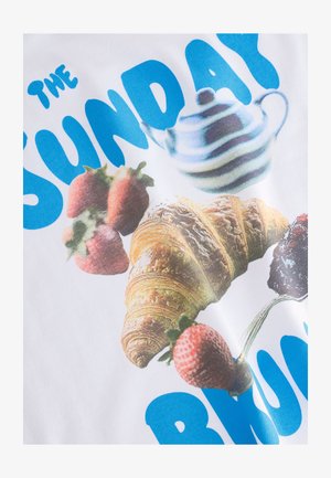 Hvid t-shirt med et grafisk design med blå tekst "THE SUNDAY BRUNCH," jordbær, en brun croissant og en stribet tekande.