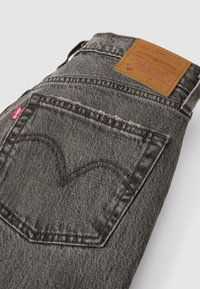 Jean Levi's gris plié montrant la poche arrière avec couture signature, étiquette rouge Levi's et patch en cuir marron de la marque.