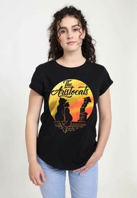 Sort t-shirt med et farverigt grafisk motiv af to katte på et tag med teksten "The Aristocats", sat mod en solnedgangsbaggrund.