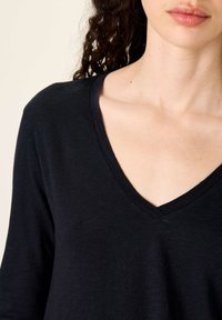 Must tekstuuriga must V-kaelusega pluus, millel on pikad varrukad ja lõdvestunud lõige. Puhtad õmblused ja lihtne disain ilma mustriteta.