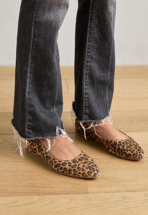 Leopardmønstret flade sko med spids tå, lavet af blødt stof; parret med jeans i mørkegrå med frynset kant. Trægulv baggrund.