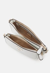 Hvid læder crossover taske med to lynlåslommer, guldfarvet hardware og beige stofforing med "GUESS" logo.