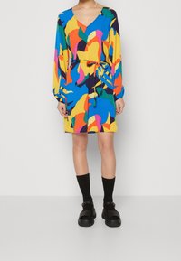 Robe multicolore avec un décolleté en V et des manches longues, dotée d'une taille à cordon. Les couleurs comprennent le bleu, le jaune, le vert, le rose et des accents noirs.