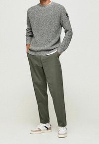 Grauer Strickpullover, lockere Passform, strukturiertes Muster. Olivgrüne Chinos, weiter Schnitt, kombiniert mit weißen Sneakers mit beigen und schwarzen Akzenten.
