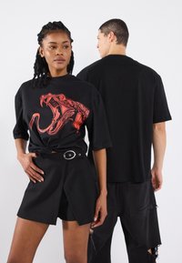 Black oversized t-shirt featuring a red snake graphic on the front. Model paired with black high-waisted shorts with a belt detail.