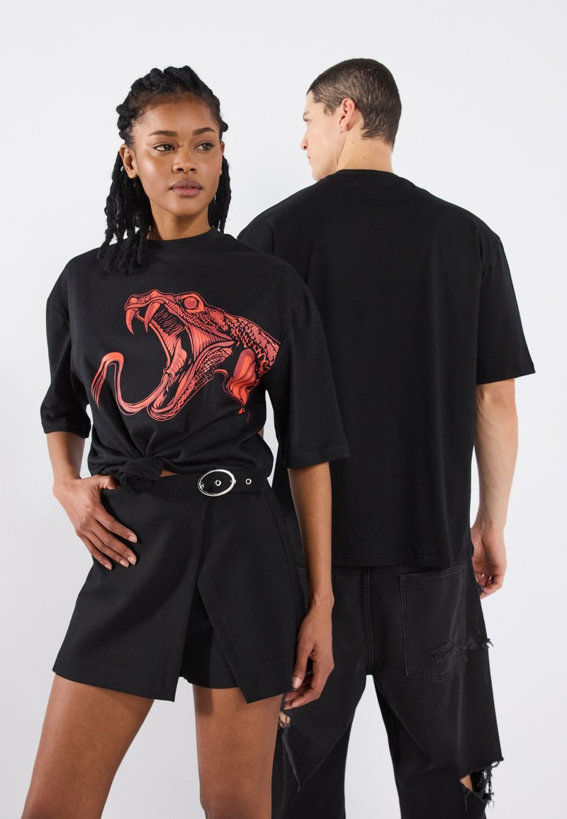 Black oversized t-shirt featuring a red snake graphic on the front. Model paired with black high-waisted shorts with a belt detail.