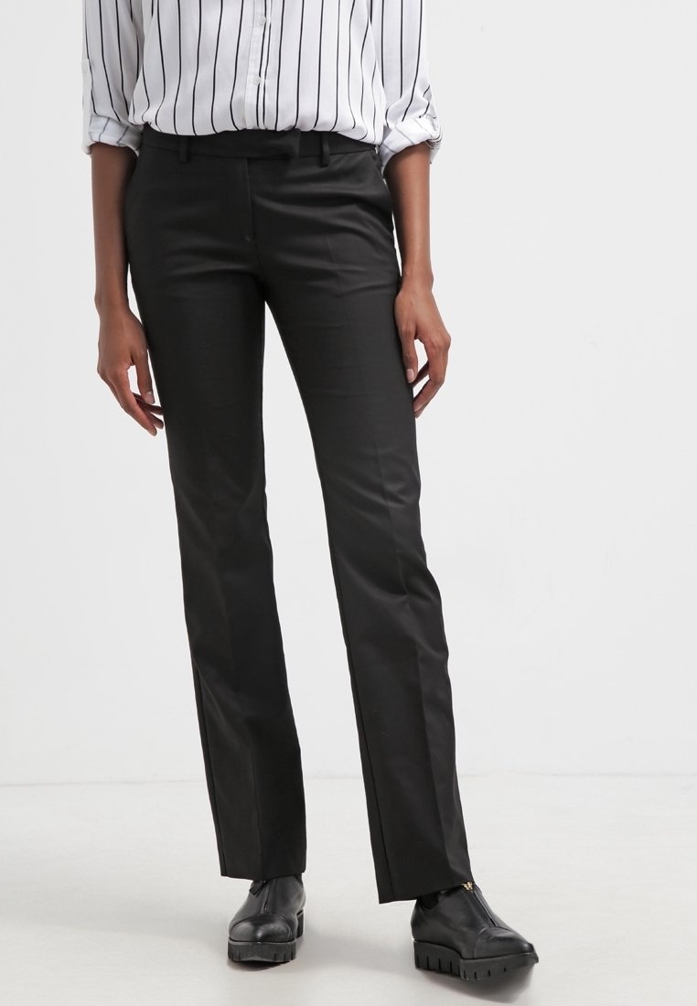 Pantalon noir sur mesure avec une coupe droite, confectionné dans un tissu lisse. Associé à une chemise blanche à rayures boutonnée et à des chaussures noires.