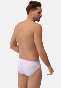 Hvide bomuldstrusser med en tynd rød linning, vist på en mand set bagfra, der fremhæver en glat tekstur og tætsiddende design.