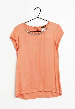 Blusa corallo a maniche corte con decorazioni gioiello lungo lo scollo rotondo appesa a una gruccia nera su sfondo bianco.