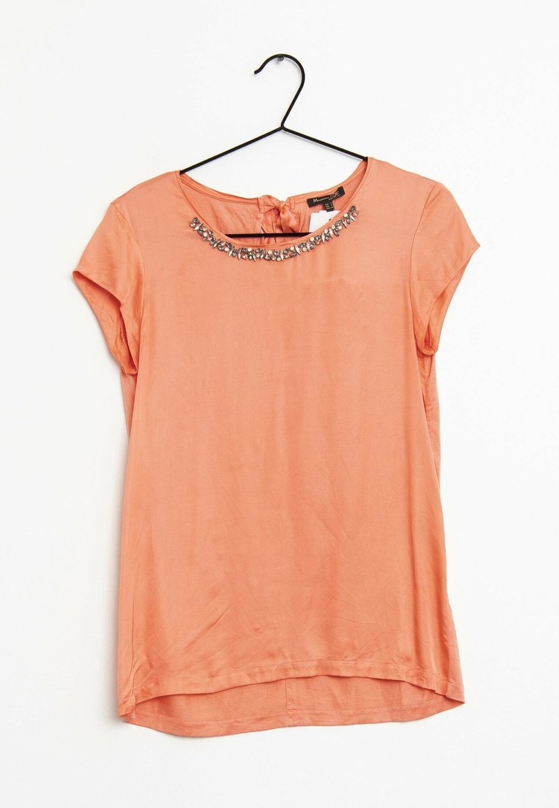 Blouse corail à manches courtes avec des embellissements bijoux le long du col rond, suspendue sur un cintre noir contre un fond blanc.