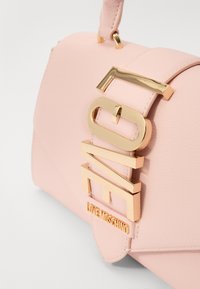 Rosa läderväska med en strukturerad design. Har en framträdande logotyp i guldton och remaccent, slät textur och magnetisk stängning.