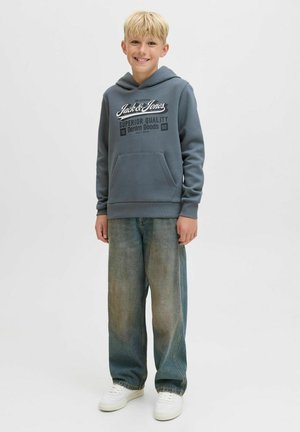 Sweat à capuche gris avec une poche frontale, arborant un texte graphique blanc. Un pantalon en denim bleu délavé, taille ample, et des baskets blanches complètent la tenue.