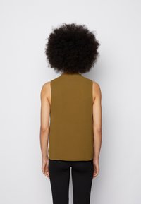 Top sem mangas, verde-oliva, com um corte descontraído, apresentando um decote redondo e uma textura suave, acompanhado de leggings pretas.