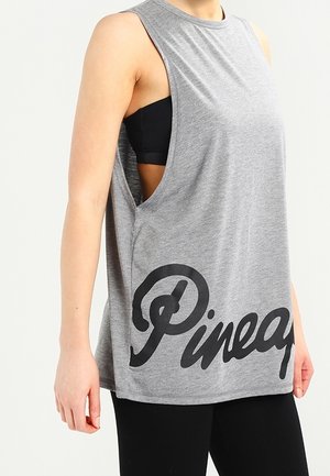 Débardeur gris sans manches avec de grandes emmanchures porté par-dessus un soutien-gorge de sport noir, avec un texte en cursive noire "Pineap" près de l'ourlet.