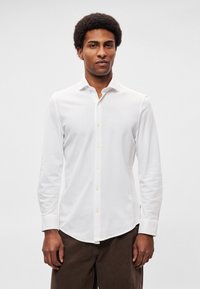 Valge pikkade varrukatega särk, valmistatud pehmest kangast, millel on nööbitav esikülg, ümaralt lõigatud serv ja heledad nupud.