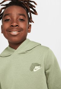 Hanorac Nike verde cu o textură moale, având glugă cu șnur și un logo alb pe piept. Design simplu, croială lejeră.