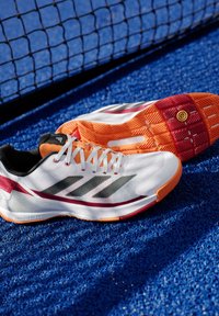 Witte sport schoenen met grijze strepen, oranje accenten en een gestructureerde zool. Voorzien van een bovenwerk van mesh, vetersluiting en een gevoerd ontwerp.