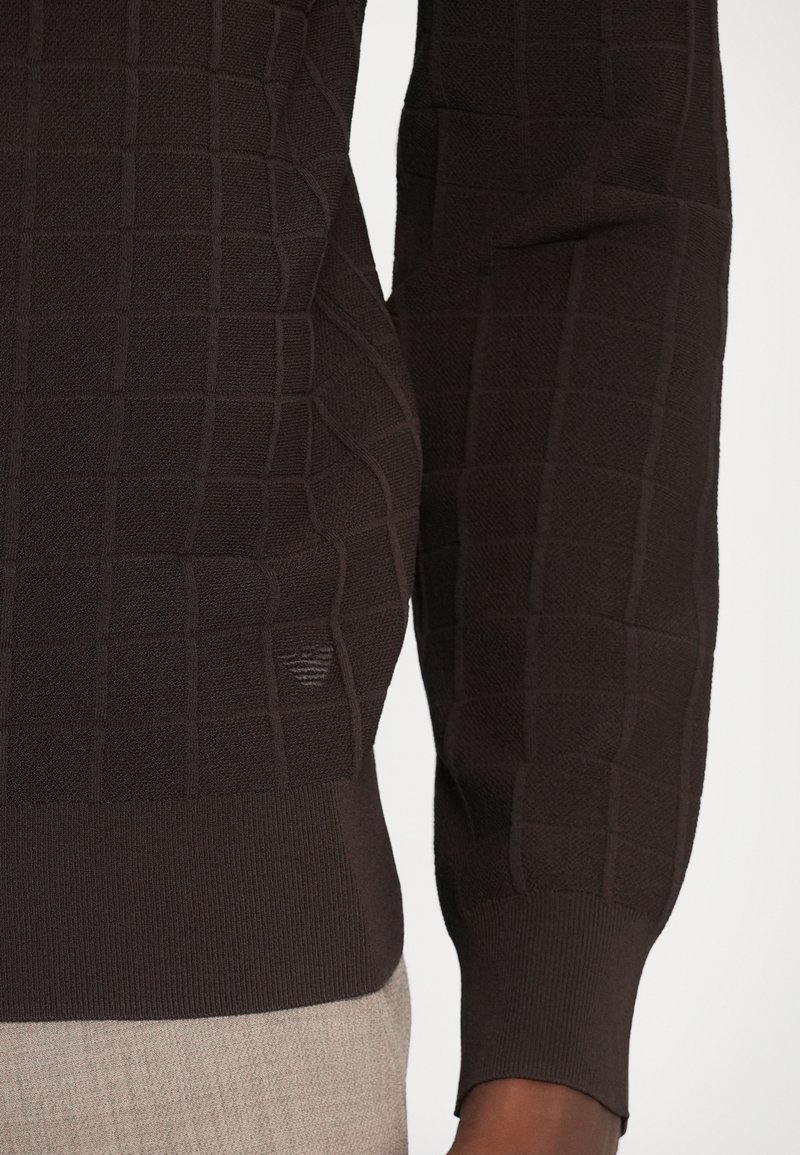 Sort strikket sweater med et tekstureret firkantet mønster, ribbede manchetter og nederkant samt en diskret logo detalje nær taljen.