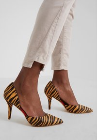 Schnürstiefeletten mit einer schwarz-gelben Tigerstreifenmuster, mit einem Stiletto-Absatz und einem roten Innenakzent.