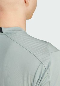 Lys grå træningsskjorte med tekstureret skulderpanel, der har et glat stof og en tætsiddende pasform. Skulderen har et diskret stribet mønster.