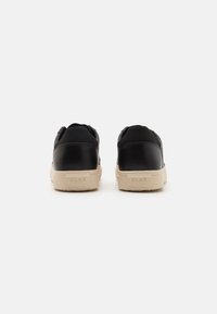 Sorte sneakers med en glatt læreroverdel, beige gummisåle, og minimalistisk design med sømmer og merkevare på hælen.