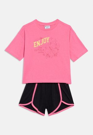 Różowy T-shirt z krótkim rękawem z napisem „CIESZ SIĘ małymi rzeczami” i kwiatowym wzorem, zestawiony z czarnymi szortami z różowym obszyciem.