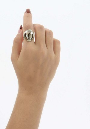 Hand met een lichte huidtint die een grote, glanzende zilveren ring draagt aan de middelvinger tegen een effen witte achtergrond.