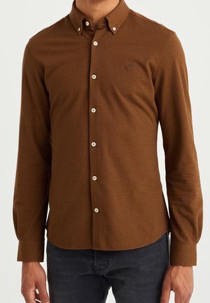 Camisa marrón de manga larga con botones blancos y pequeño logo bordado en el pecho, combinada con pantalones gris oscuro.