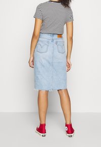 Gonna di denim azzurro chiaro con orlo sfrangiato, due tasche posteriori e una patch in pelle, abbinata a una maglietta a righe bianche e nere e sneaker rosse.