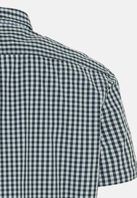 Camicia a maniche corte in tessuto a quadri bianchi e neri, con colletto a punta e cuciture precise. Tessuto di cotone con texture liscia.