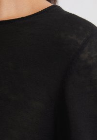 Zwart textiel met een close-up van een ronde halslijn en zichtbare stiksels, die een lichte en zachte uitstraling benadrukt.