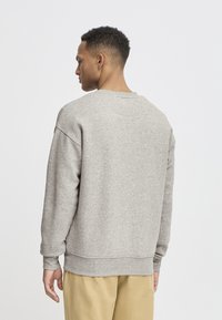 Lys grå hettegenser laget av mykt stoff, med rund hals, lange ermer og ribbestrikkede mansjetter. Tilbake viser et enkelt, sømløst design.
