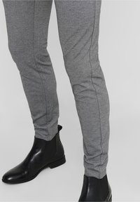 Pantalons slim gris texturé avec des détails de couture visibles, associés à des bottes chevilles en cuir noir dotées de panneaux élastiques sur les côtés.