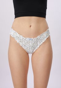 Donna che indossa un bikini bianco a fiori con volant e un top nero corto su uno sfondo chiaro uniforme.