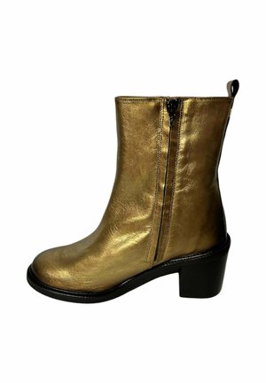 Botín de tobillo de cuero sintético dorado con tacón cuadrado, cremalleras laterales y textura suave. Presenta una puntera redondeada y una suela negra en contraste.