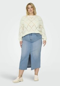 Lahki, pleteni krema pulover z diamantskimi izrezi, v kombinaciji z visokim modrim jeans krilom, ki ima sprednji razporek. Krema loaferji dopolnjujejo videz.