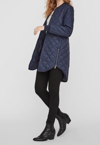 Vadderad marinblå ytterjacka med dragkedja i sidan, rund krage och ribbade muddar, tillsammans med åtsittande svarta byxor och stövletter.