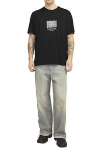 Camiseta de algodón negra con el texto gráfico blanco "PARK SLOPE" en el pecho; combinada con unos jeans de mezclilla gris claro de corte holgado y zapatos negros.