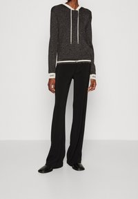 Haut à capuche noir pailleté avec un cordon blanc et des poignets, associé à un pantalon large noir. La tenue présente un détail de ceinture contrastant.