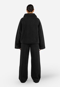 Giacca oversize in fleece nera con colletto alto, vestibilità ampia e maniche larghe, abbinata a pantaloni neri a gamba larga coordinati.
