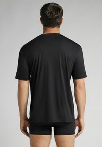 Černé tričko s krátkým rukávem a kulatým výstřihem, hladká textura a uvolněný střih, nošené přes černé boxerky na neutrálním pozadí.