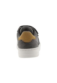 Zapatilla de ante gris con suela de goma blanca, que presenta un acento de ante dorado en el talón y un bucle para facilitar su uso. Diseño plano.