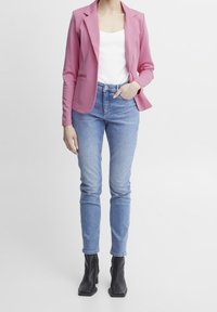 Pink blazer over a white top, paired with light blue fitted jeans and black heeled ankle boots. Smooth fabric, tailored design, and slim fit.