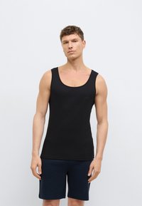 Čierny tielkový top s okrúhlym výstrihom, rebrovanou textúrou a jemným logom na hrudi; v kombinácii s tmavomodrými šortkami, model stojí na svetlom pozadí.