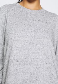 Sweatshirt gris en tissu texturé, avec un col rond et des manches légèrement bouffantes ornées d'un motif moucheté subtil.