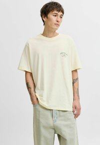 Gaišdzeltena kokvilnas T-kreklu ar īsām piedurkn�ēm, apaļu izgriezumu un mazu zaļu grafisko logo kreisajā krūtī. Mīksta tekstūra, brīvi pieguļoša piegriezums.