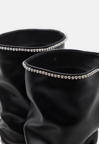Botines negros de cuero con un diseño holgado, que presentan un borde superior decorado con detalles de strass plateados para aportar textura y detalle.