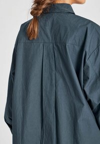 Dunkelblauses übergroßes Shirt aus leichtem Stoff; verfügt über einen Rückenschlitz und eine weiche Textur. Kragen Design mit langen Ärmeln.