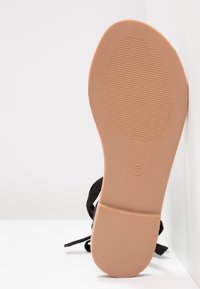 Semelle d'une sandale noire avec une semelle en caoutchouc beige, taille 37 indiquée, montrant une texture de grip horizontale sur la zone de la plante du pied.