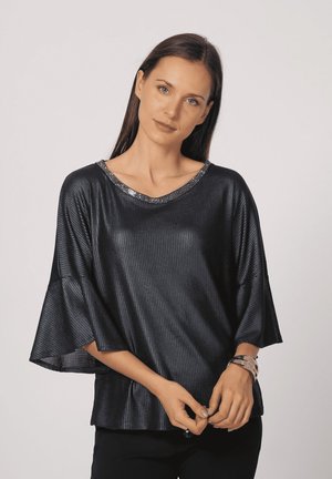 Top negro con relieve, de corte holgado y mangas anchas, con un escote brillante de lentejuelas. Textura suave, combinado con pantalones oscuros.